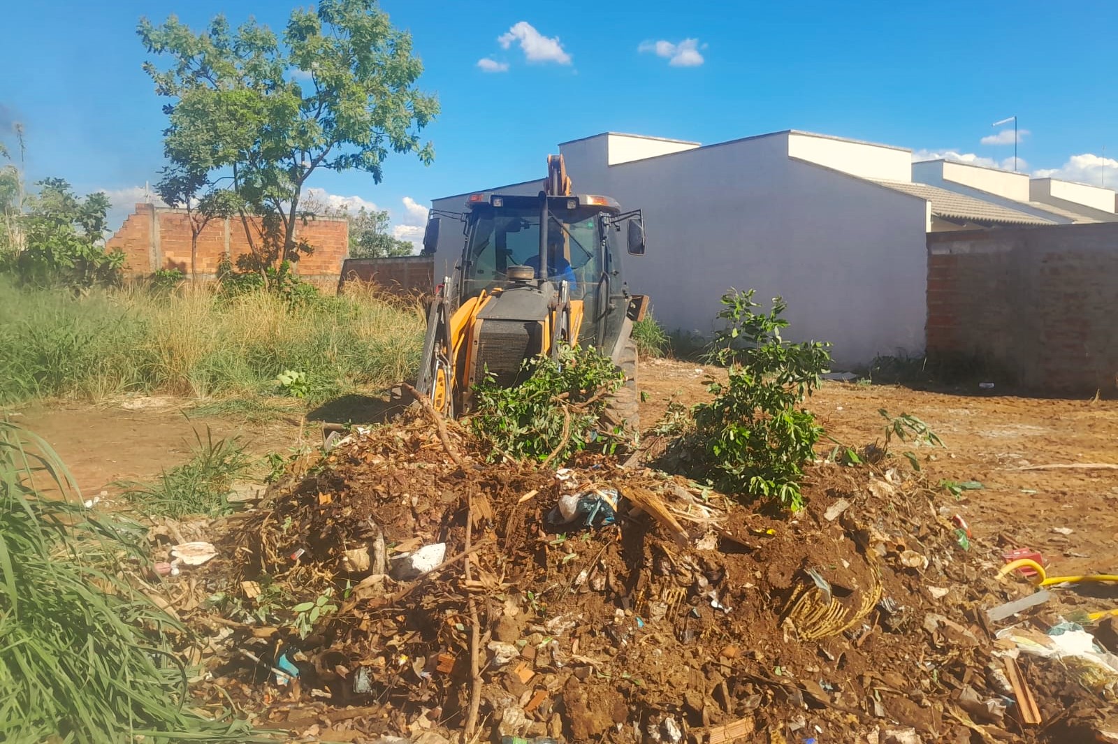 Máquina retroescavadeira retirando entulho de lote no distrito de Buritirana
